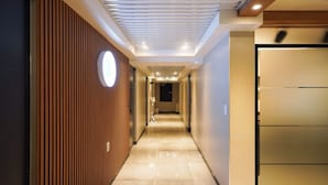 A modern hotel corridor with a wooden panel wall, a circular light fixture, and a door at the end. - Han stay (Seoul)
