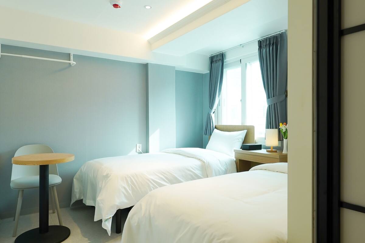 Ein Hotelzimmer mit zwei Betten, einem runden Tisch und einem Fenster mit Vorhängen.