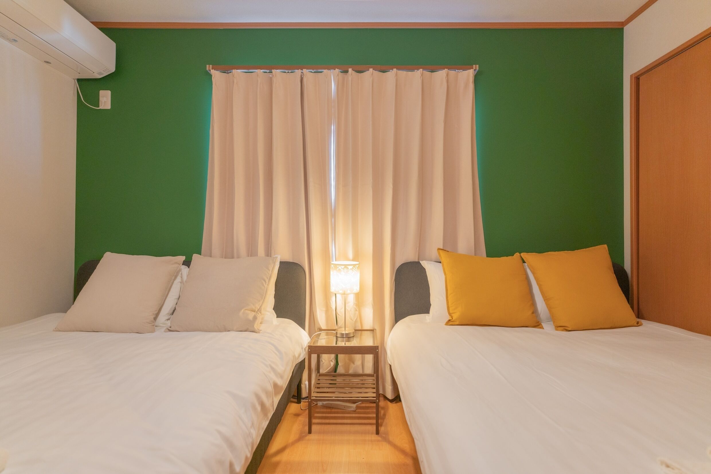 A hotel room with two beds, a nightstand with a lamp, and a window with curtains.