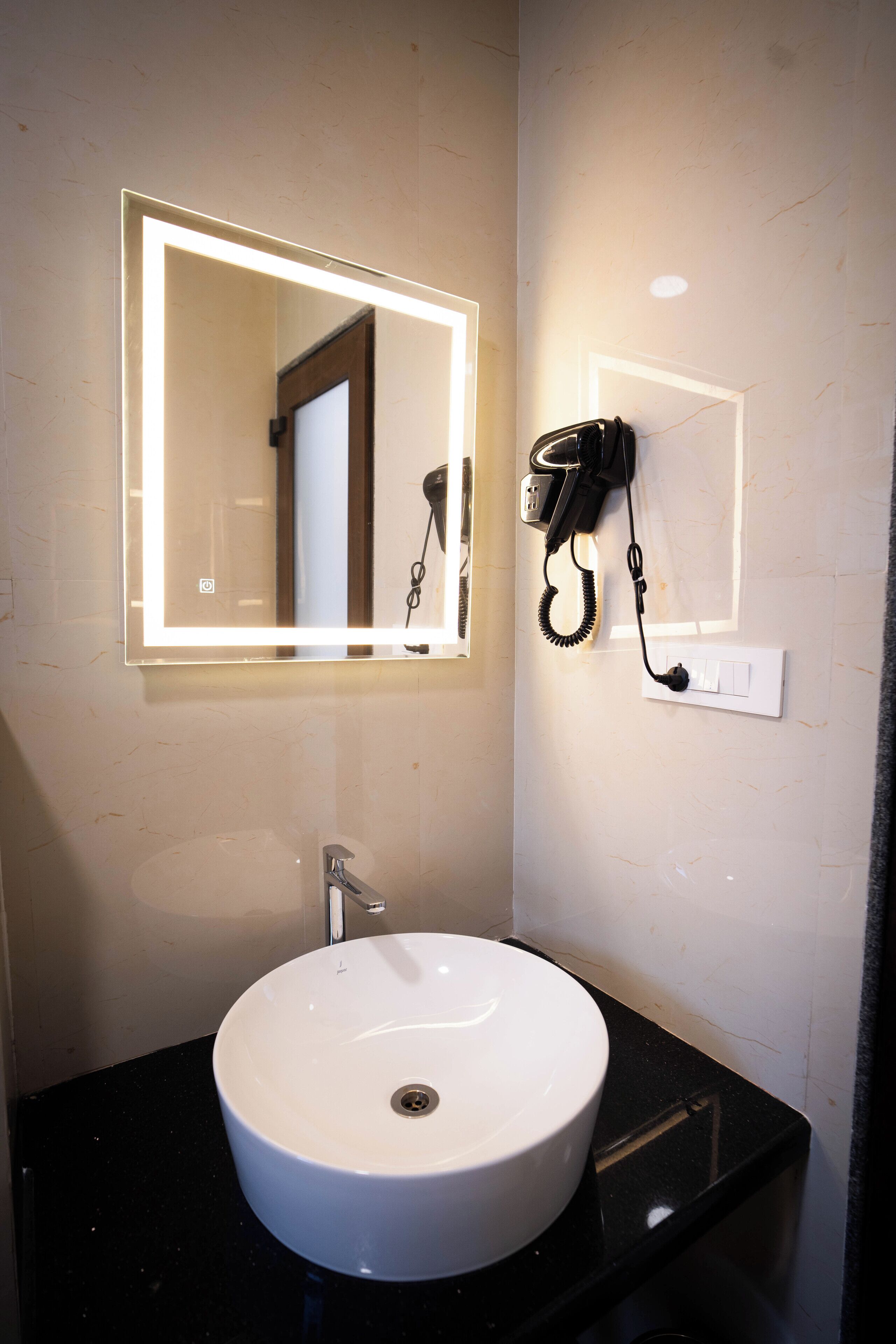 Un baño con un lavamanos blanco, un espejo con bordes iluminados y un secador de pelo montado en la pared.
