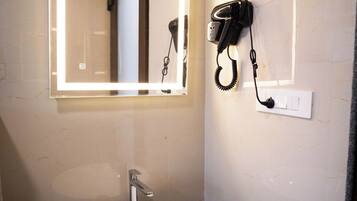 Ett badrum med ett vitt handfat, en spegel med belysning runt kanten och en hårtork som är monterad på väggen.