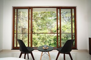 Ein Zimmer mit einem großen Fenster, zwei schwarzen Stühlen und einem kleinen Tisch mit einer Tasse.