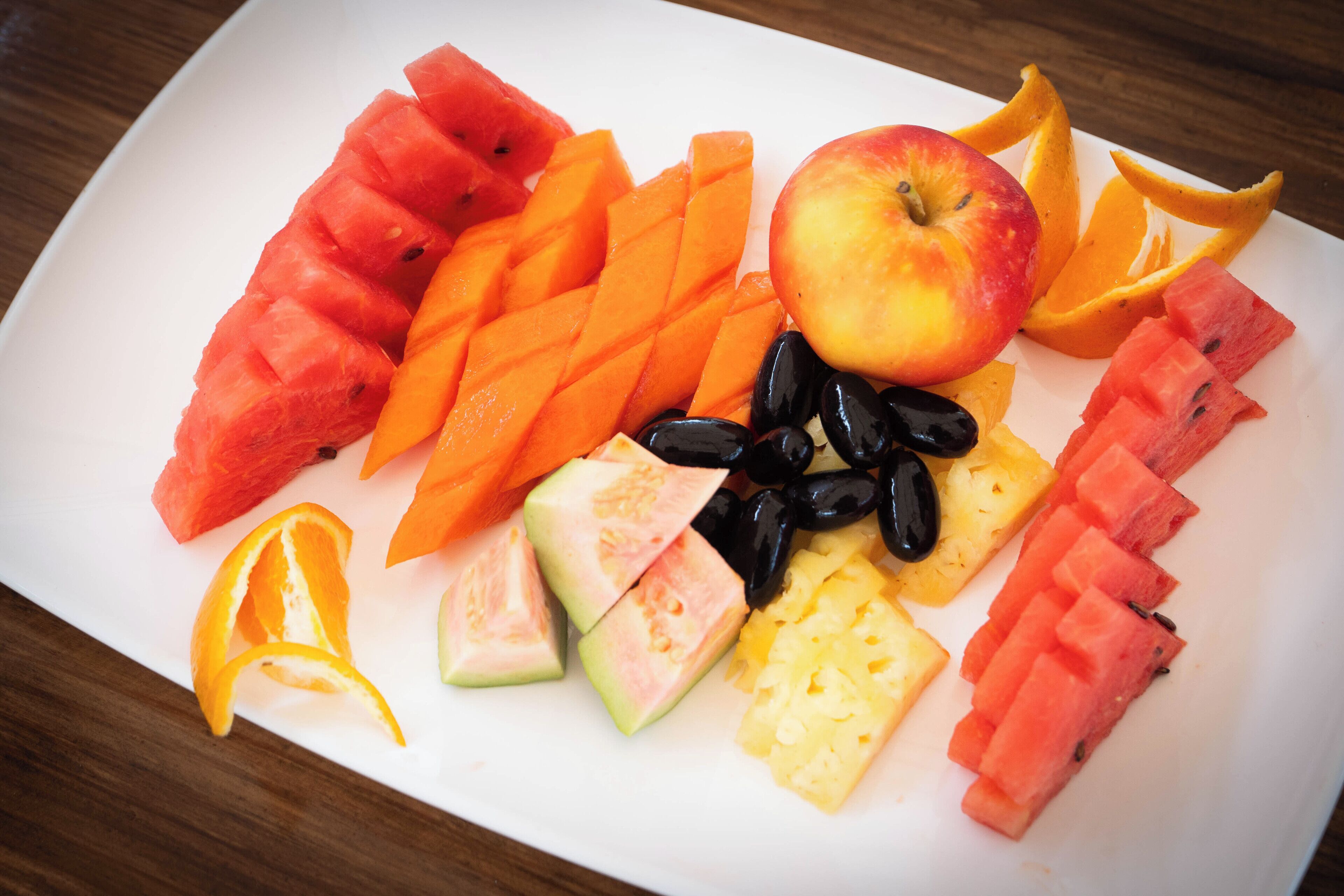 Un plato blanco con varias frutas, entre ellas sandía, piña y gajos de naranja.