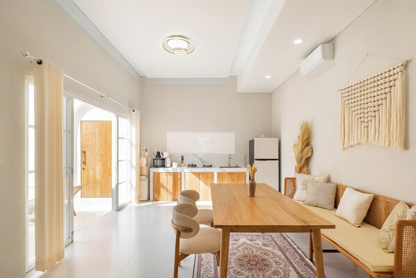 A modern kitchen with wooden cabinets, a central island, and a dining area with a wooden table and chairs. - Private Pool Villa Ahana by OriVista (Canggu)