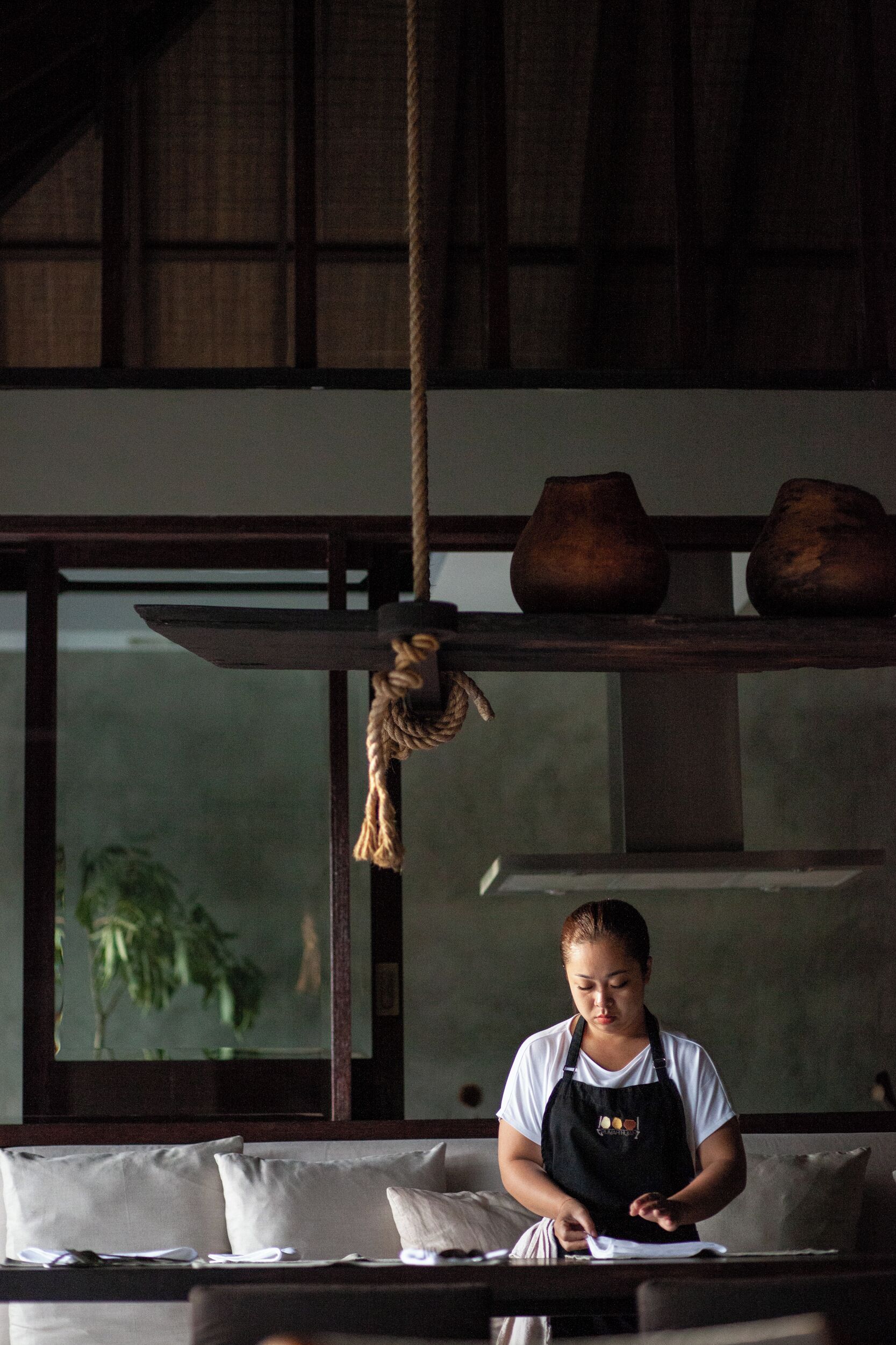 A person seated at a table with a notebook, in a room with a wooden ceiling and a large window.