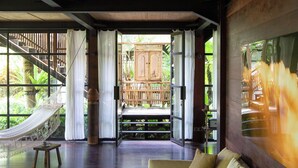 A spacious room with a large bed, a hammock, and a view of a wooden deck and lush greenery. - Rumah Hujan (Ubud)
