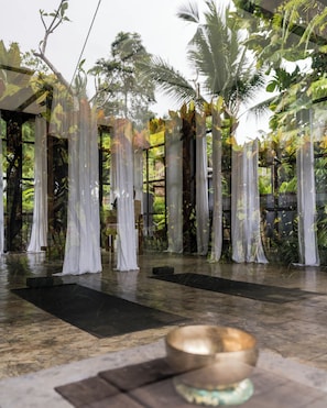 Un espace intérieur paisible, équipé d’un tapis de yoga, d’un bol de méditation et d’une cloison en verre agrémentée de rideaux légers.