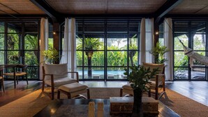 A spacious room with large windows, a hammock, and a view of a pool. - Rumah Hujan (Ubud)