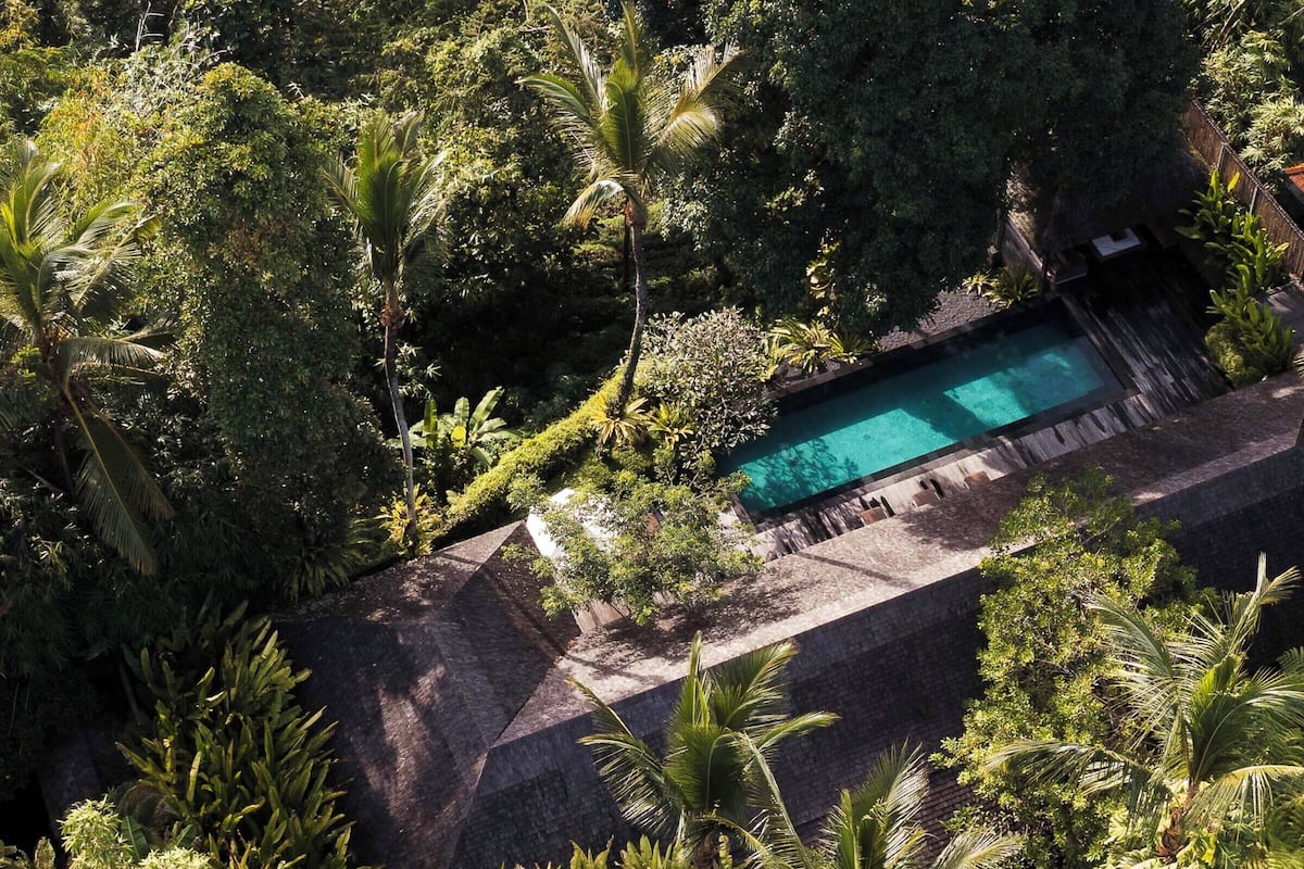 Eine Vogelperspektive zeigt ein Resort mit einem Schwimmbad, umgeben von üppiger Vegetation und Palmen.