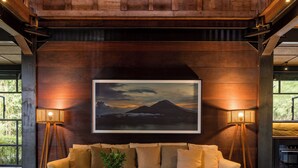 A cozy living room with a sofa, coffee table, and two chairs. A framed picture hangs above the sofa, and there are two floor lamps on either side. - Rumah Hujan (Ubud)