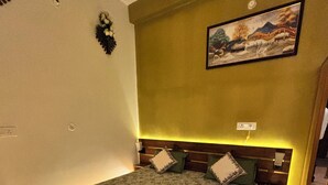 A bedroom with a large bed, a headboard with built-in lighting, a painting on the wall, and a wooden wardrobe. - Hotel Sangam Village (Karchana)