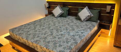 A bed with a floral-patterned bedspread, wooden headboard, bedside tables, and a wall socket.