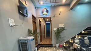 A hotel lobby with patterned flooring, a reception desk, a TV, and a staircase leading to the upper floors. - Hotel Sangam Village (Karchana)