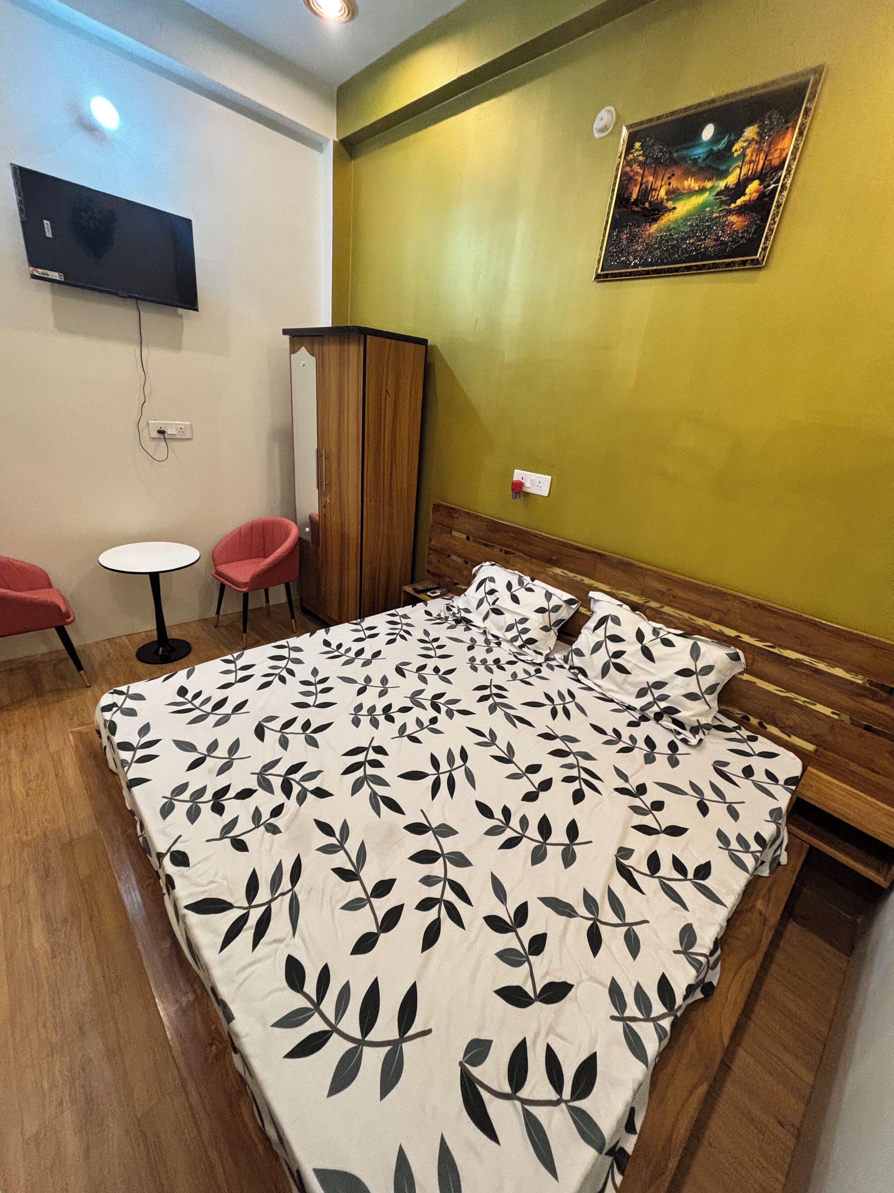 Une chambre à coucher avec un lit, deux chaises, un téléviseur et un tableau accroché au mur.