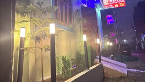 A modern hotel exterior with a neon sign, a well-lit entrance, and a landscaped garden area. - Hotel Sangam Village (Karchana)
