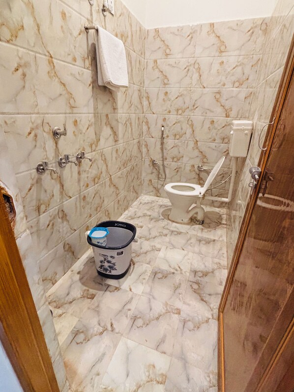 A bathroom with marble walls, a toilet, a shower, and a sink with a Joyo water heater. - Hotel Sangam Village (Karchana)
