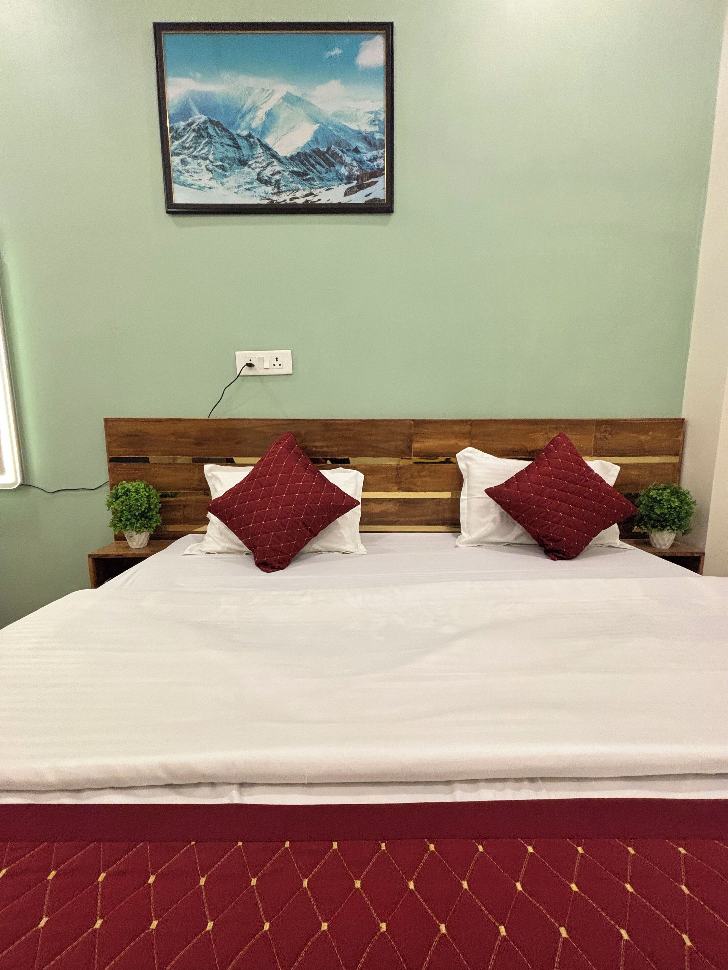 A neatly made bed with a wooden headboard, two pillows, and a red quilted bedspread.