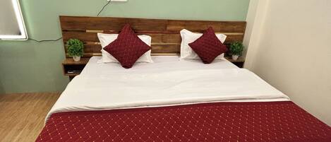 A neatly made bed with a red quilt, two pillows, and a wooden headboard. A small plant is on the nightstand beside the bed.