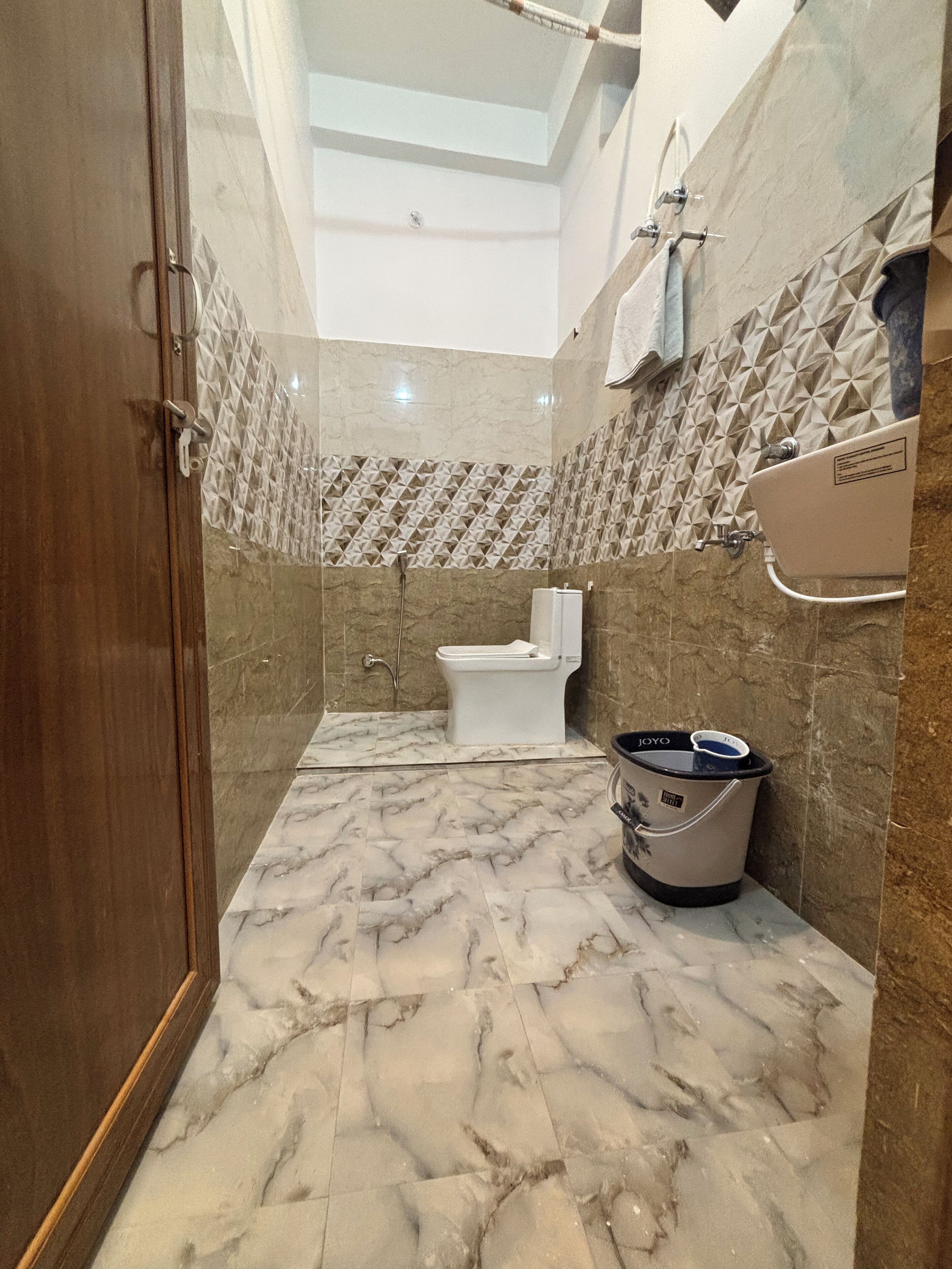A bathroom with a marble floor, a toilet, a bidet, and a bucket.