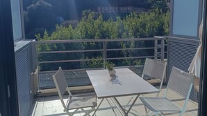Varanda com mesa e cadeiras, vista para um morro com edifícios e vegetação.