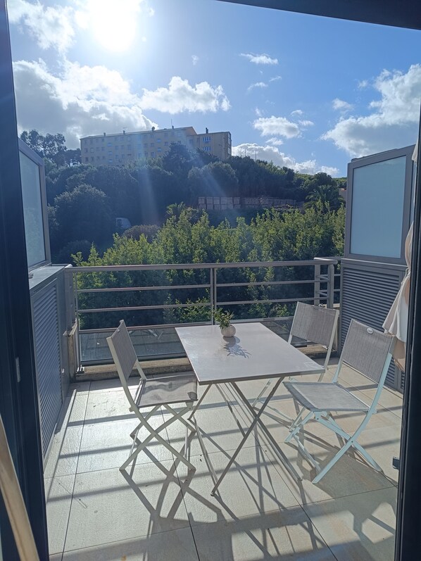 A balcony with a table and chairs, overlooking a hillside with buildings and greenery.