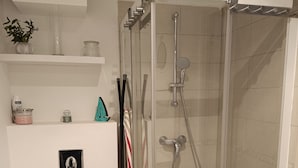 Uma casa de banho moderna com cabine de duche em vidro, sanita branca e prateleira com artigos de higiene pessoal.