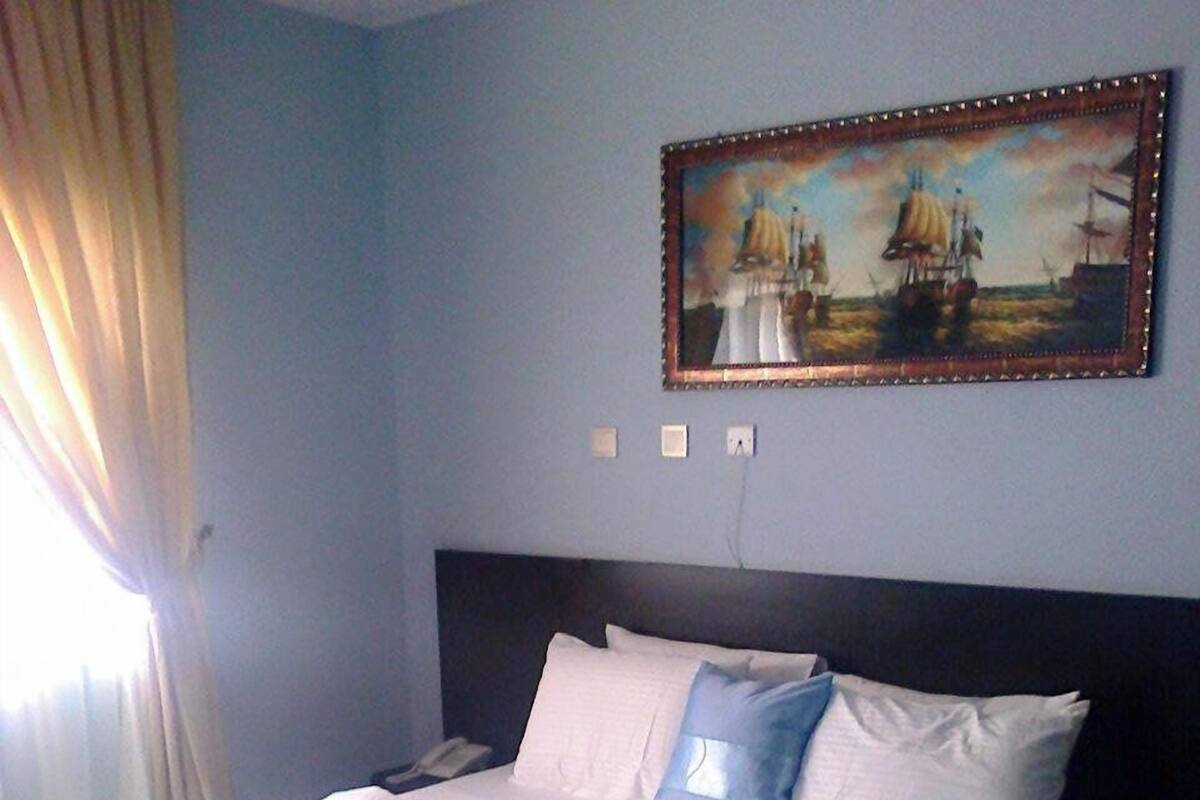 A hotel room with a large bed, a painting on the wall, and a patterned rug.