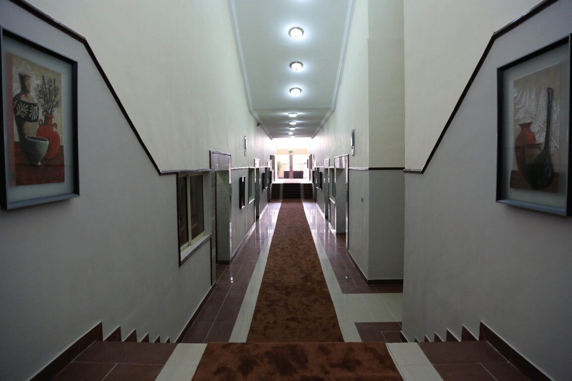 A long, narrow hallway with a patterned carpet, framed artwork on the walls, and a series of doors on one side.