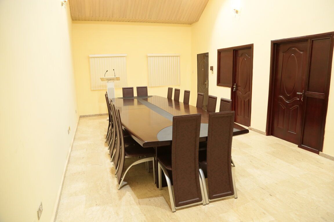 Uma sala de conferência com uma mesa comprida e cadeiras, um p úlpito e duas janelas com persianas.
