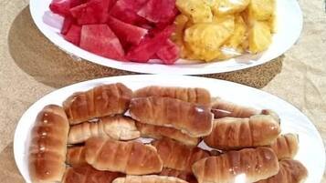 Una mesa con tres platos de comida: una ensalada, sandía y trozos de piña; un plato de cruasanes; y un plato de pan rebanado.
