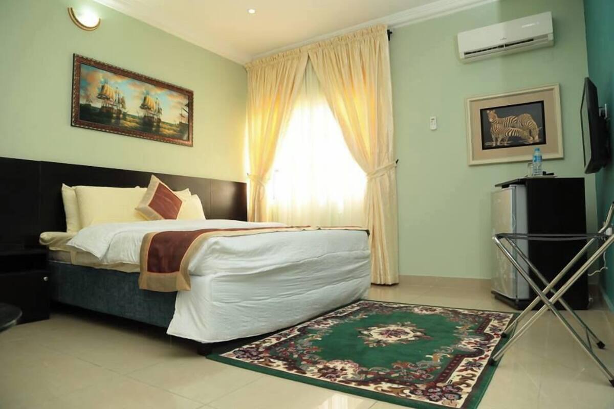 A hotel room with a bed, a desk, a chair, a TV, and a window with curtains.