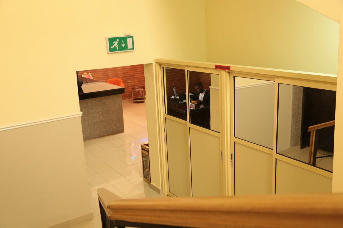 Zona de recepción de hotel con mostrador, una persona detrás y una escalera que sube a otro piso.