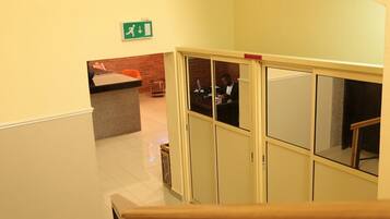 Zona de recepción de hotel con mostrador, una persona detrás y una escalera que sube a otro piso.