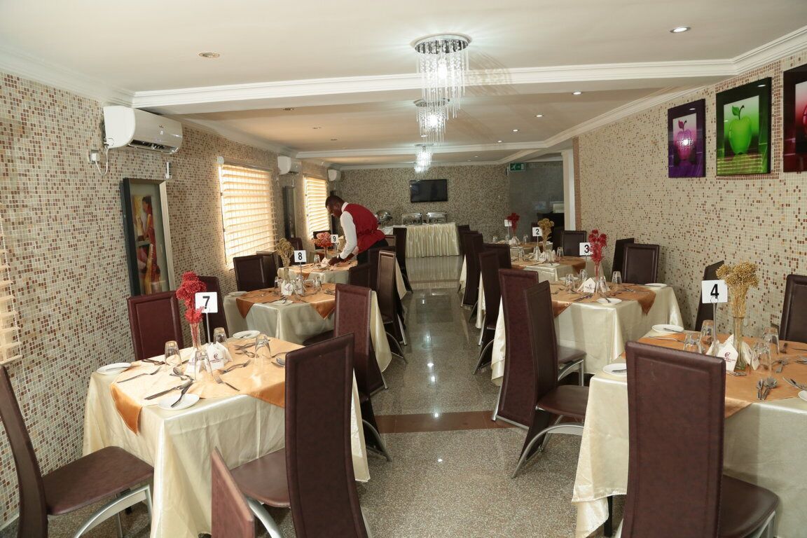 A dining area with numbered tables, a chandelier, and a person in a red apron.