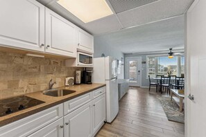 A kitchen with white cabinets, a microwave, a refrigerator, a sink, and a dining area with a table and chairs.