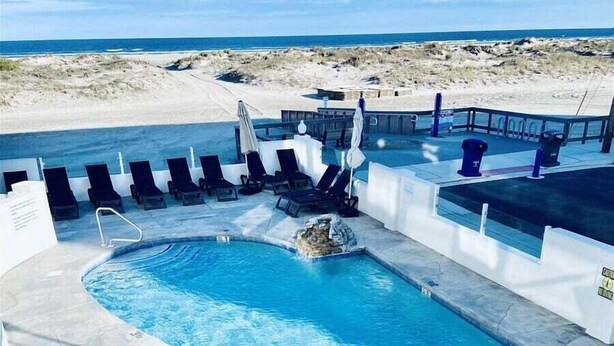 Una piscina de diseño curvo, rodeada de sillones de descanso y vista a la playa.