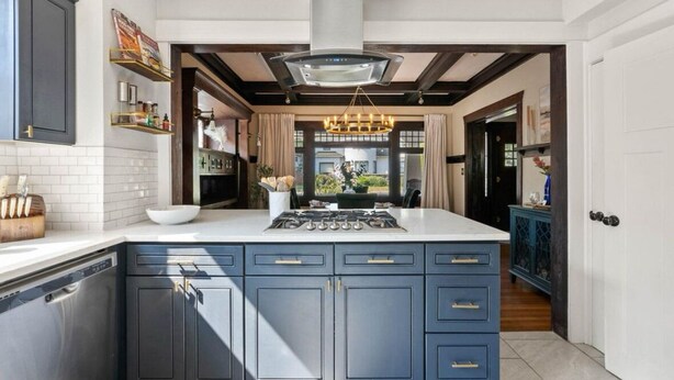 Une cuisine moderne avec des meubles de couleur bleu foncé, un îlot central doté d’une plaque de cuisson et un luminaire suspendu.