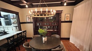 Un coin repas avec une table ronde, des chaises, un lustre, une cuisine en arrière-plan et un tapis à motifs.