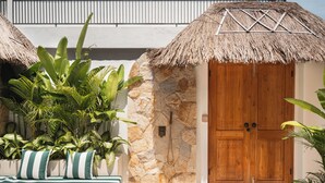 A tropical-style building with a stone wall and wooden door, surrounded by lush greenery and a thatched-roof structure. - Villa Kaia by Alfred in Bali (Canggu)