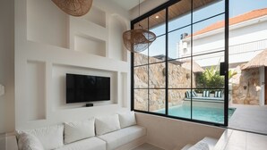 A modern living room with a large window, a flat-screen TV, and a white sofa. - Villa Kaia by Alfred in Bali (Canggu)
