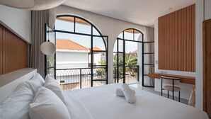 A modern hotel room with a large bed, a desk, and a view of the outside. - Villa Kaia by Alfred in Bali (Canggu)