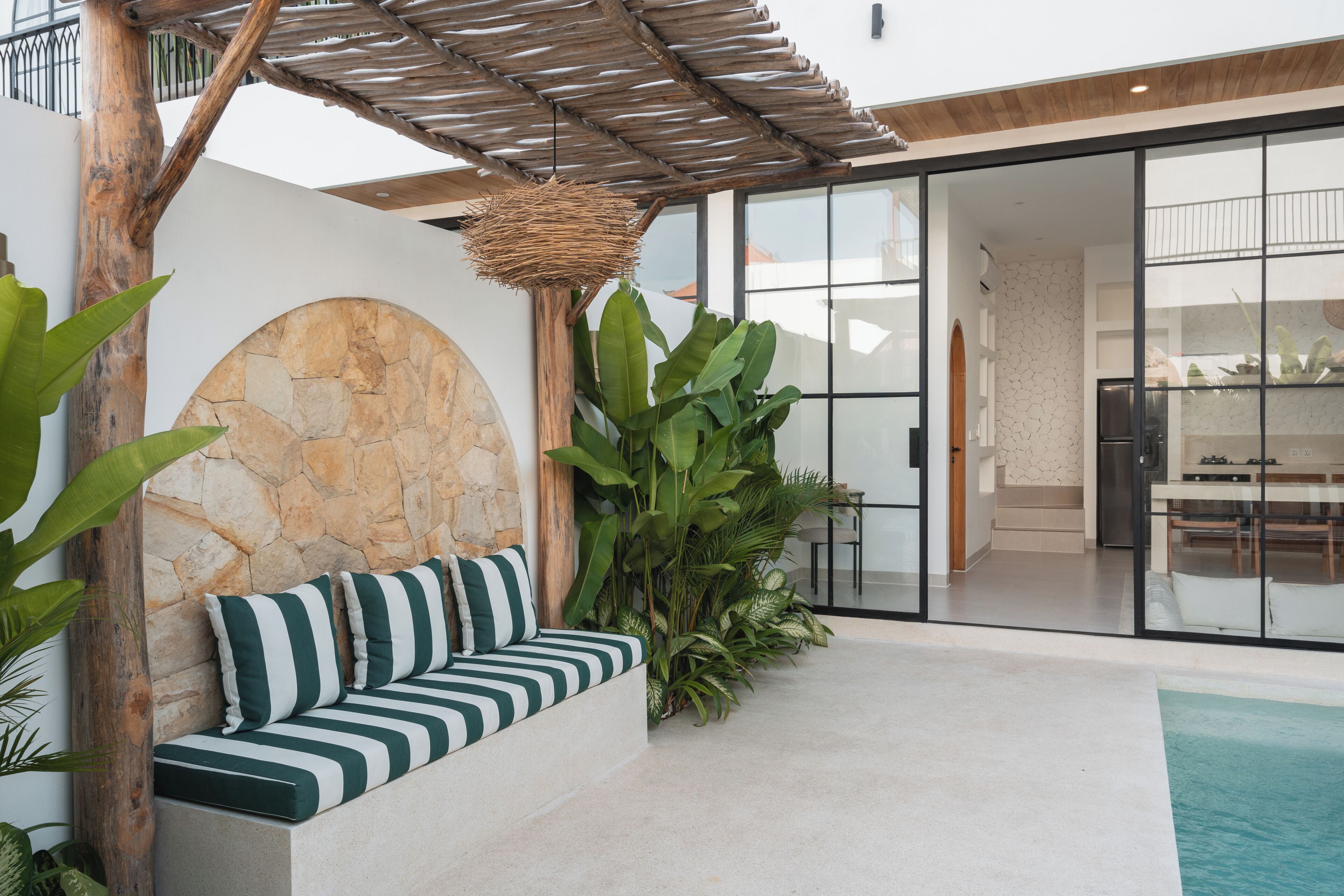 A modern outdoor seating area with a stone wall, a wooden pergola, and a large planter with tropical plants.