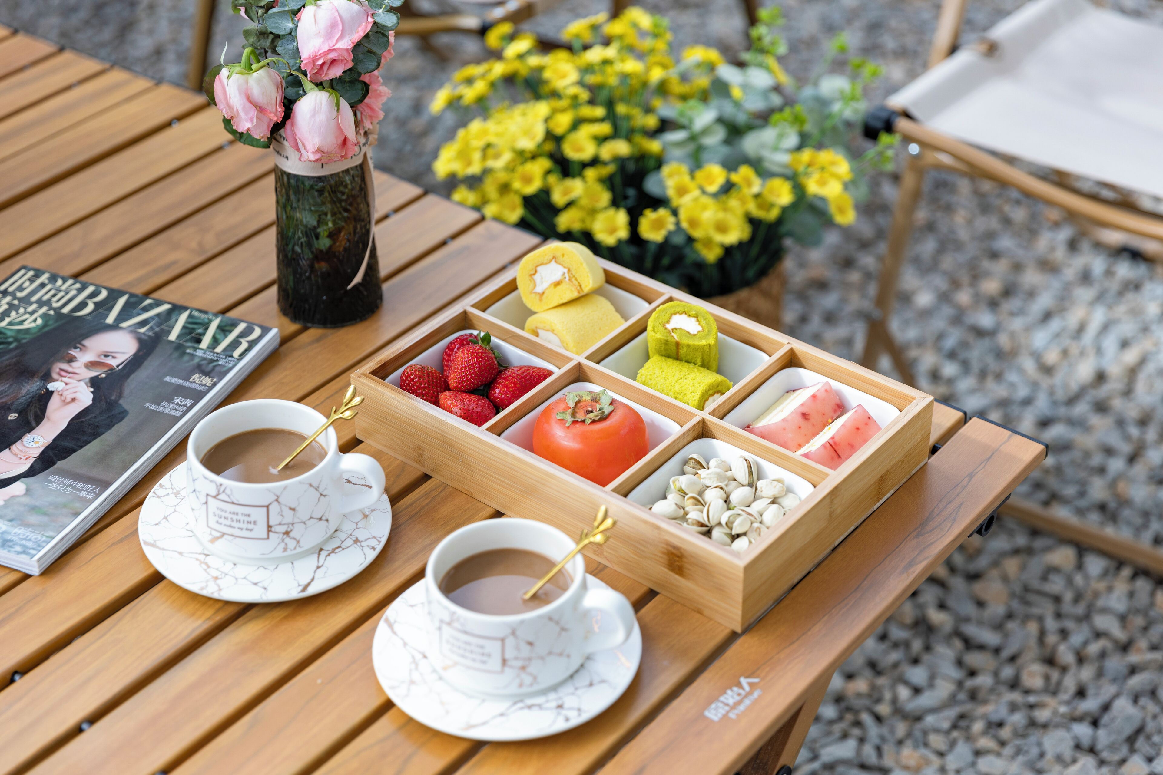Un tavolo di legno con due tazze di caffè, un vassoio con fragole, un pomodoro e pistacchi.