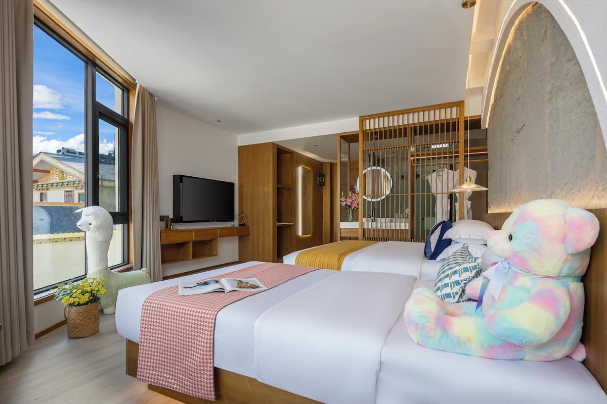 Habitación de hotel con un ventanal grande, una cama, un televisor y un osito de peluche.