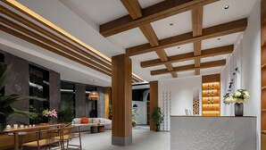 A spacious lobby with a wooden reception desk, seating area, and large windows.