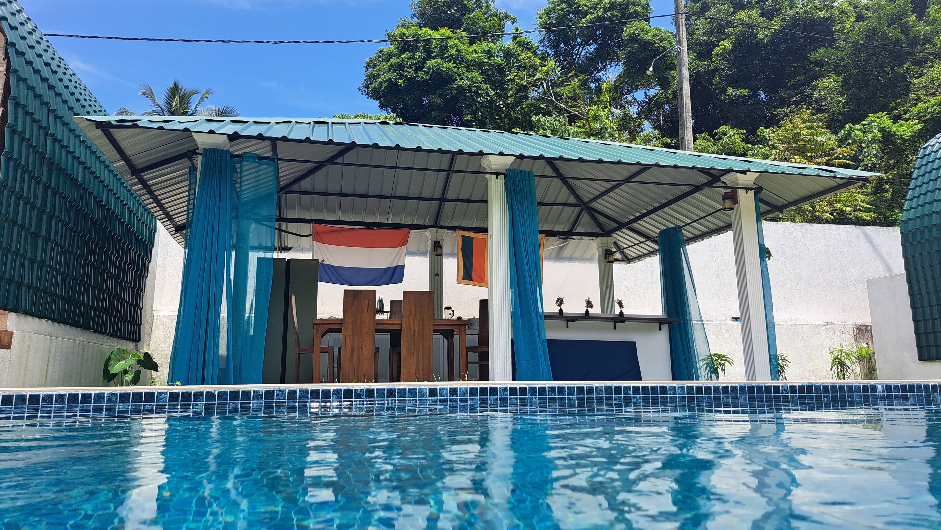 A swimming pool with a covered area, a flag, and a white wall.