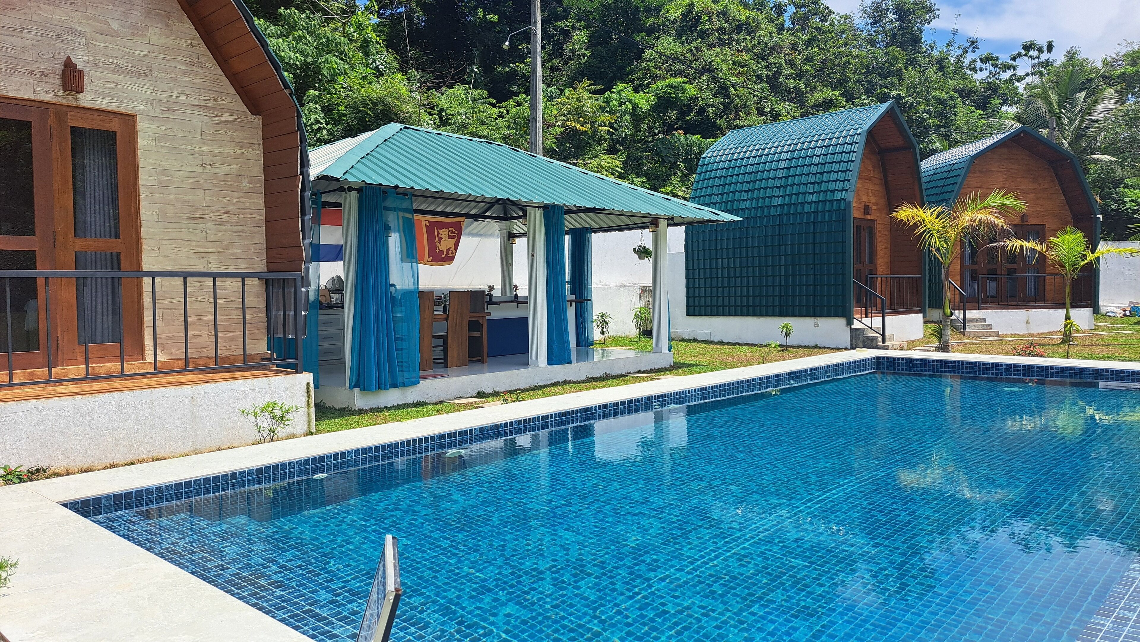Une piscine dotée d’une terrasse carrelée, d’un espace de repos couvert et de deux bâtiments adjacents surmontés de toits végétalisés.