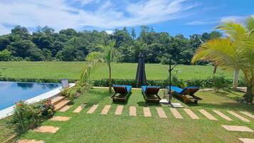 Un área junto a la piscina con sillones de descanso y una pérgola.