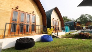 Una hilera de cabañas de madera con ventanas grandes y un balcón, un césped y un sillón de mimbre azul.