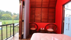 Un dormitorio con balcón, dos sillas de madera, una cama y vistas a un paisaje verde.